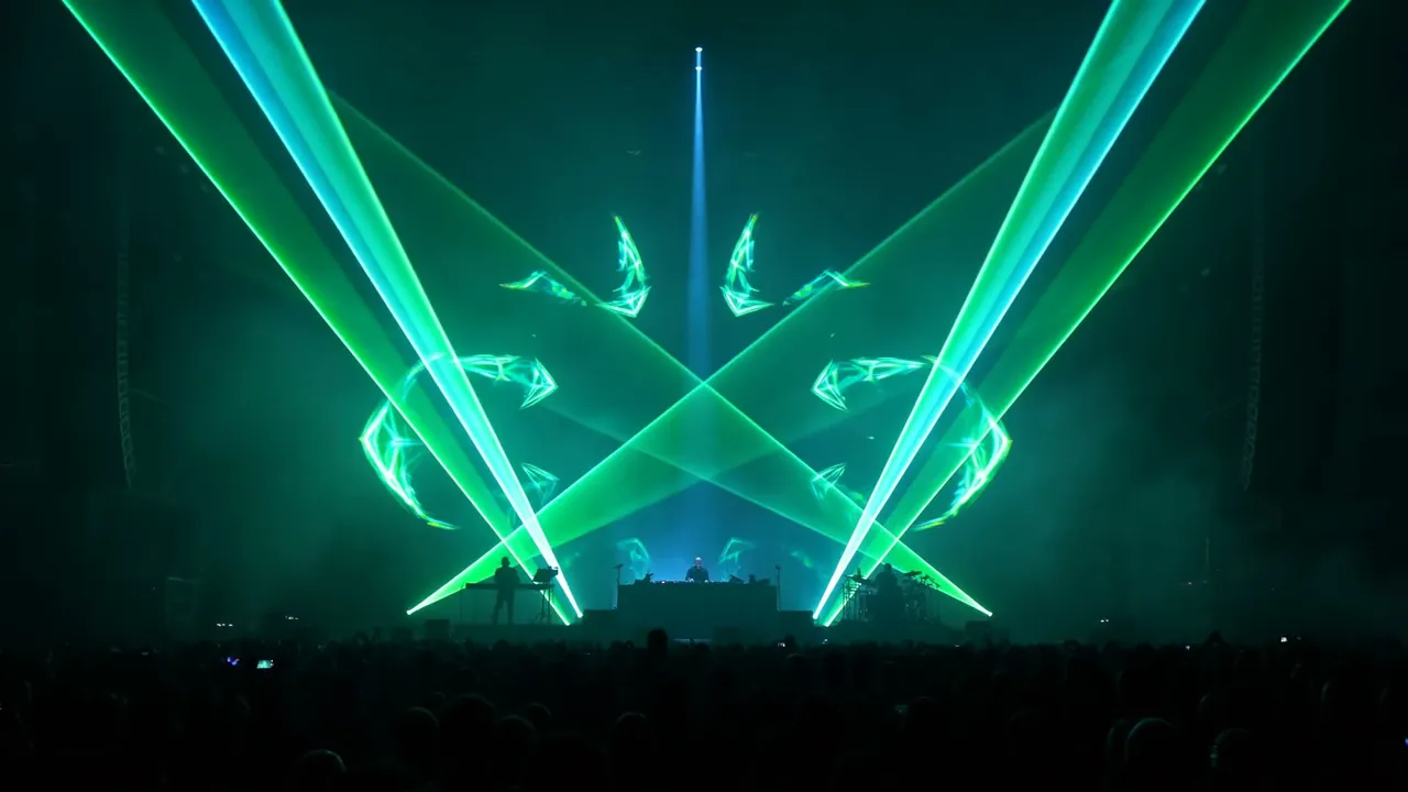 Green laser fans crossing above a stage with a single white beam overhead