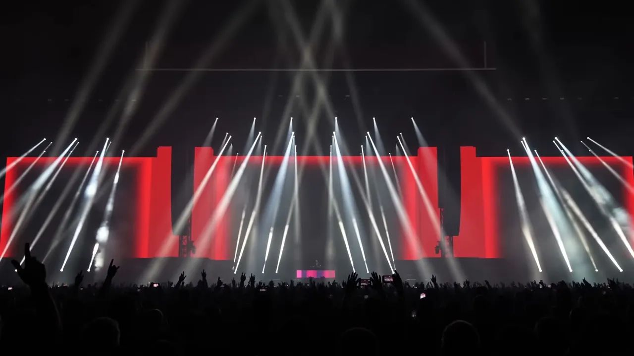 White beam wall over a red LED stage and a packed crowd